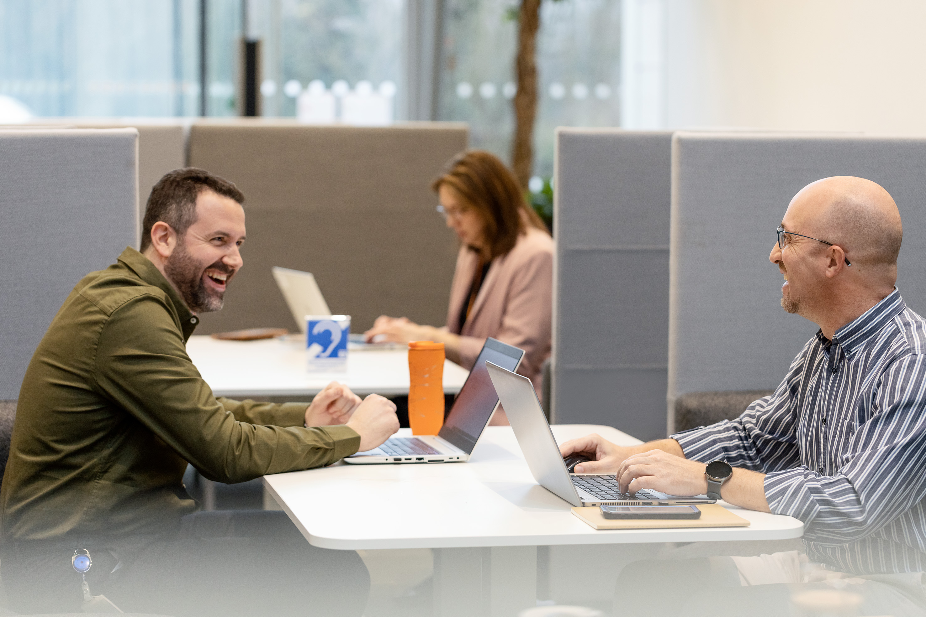 two men in discussion while working on their laptops.