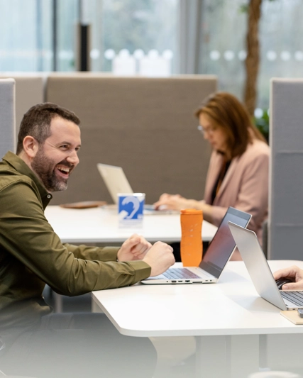 two men in discussion while working on their laptops.